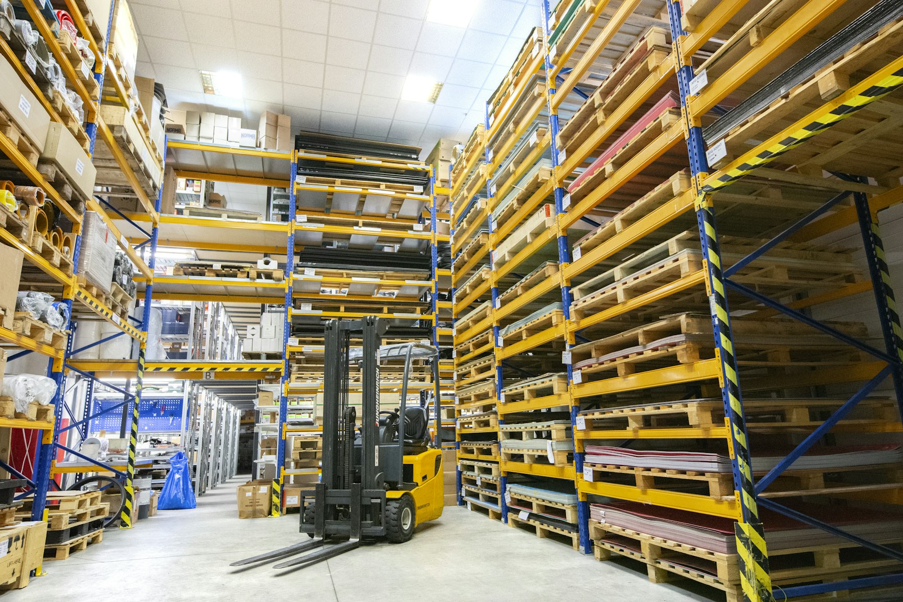 Warehouse racking filled with pallets, with a forklift in the aisle