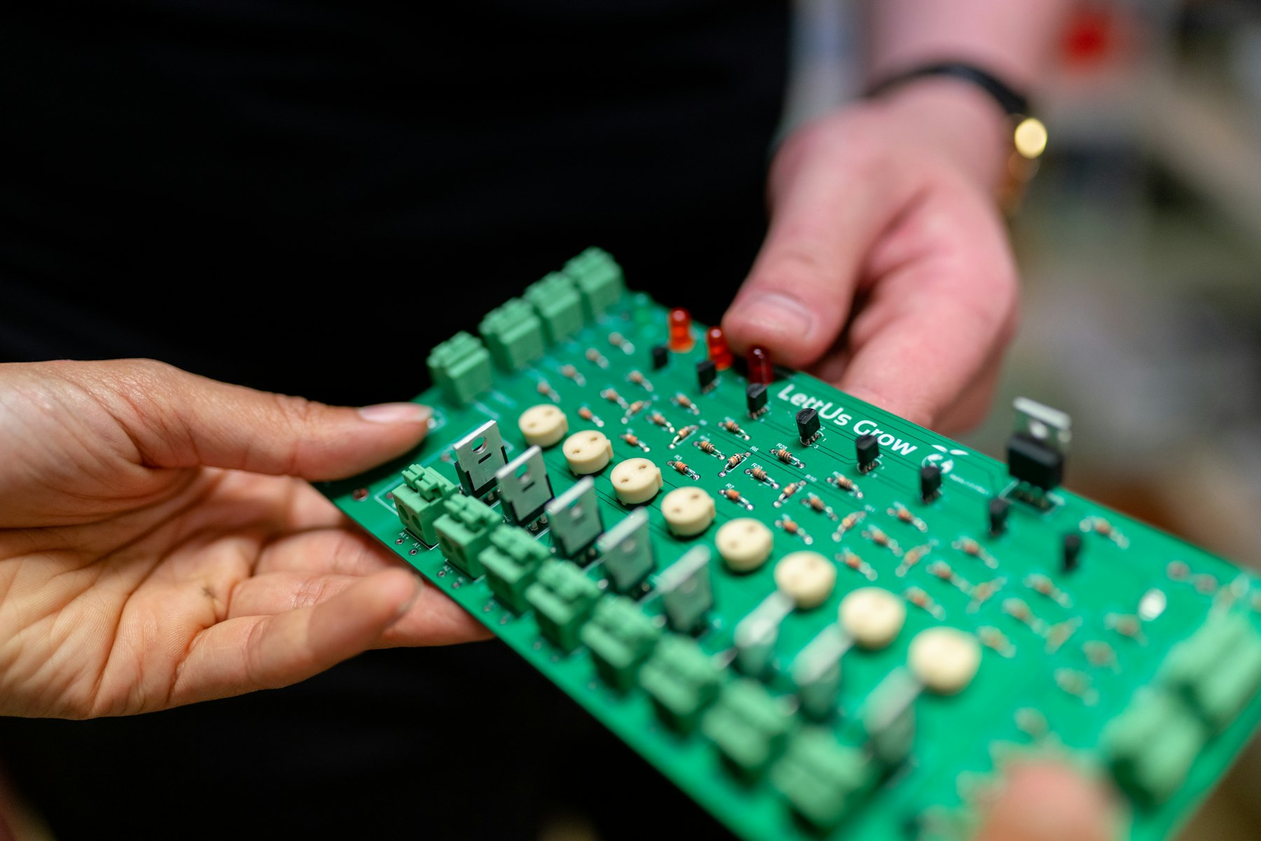 Hands holding a populated green circuit board for inspection